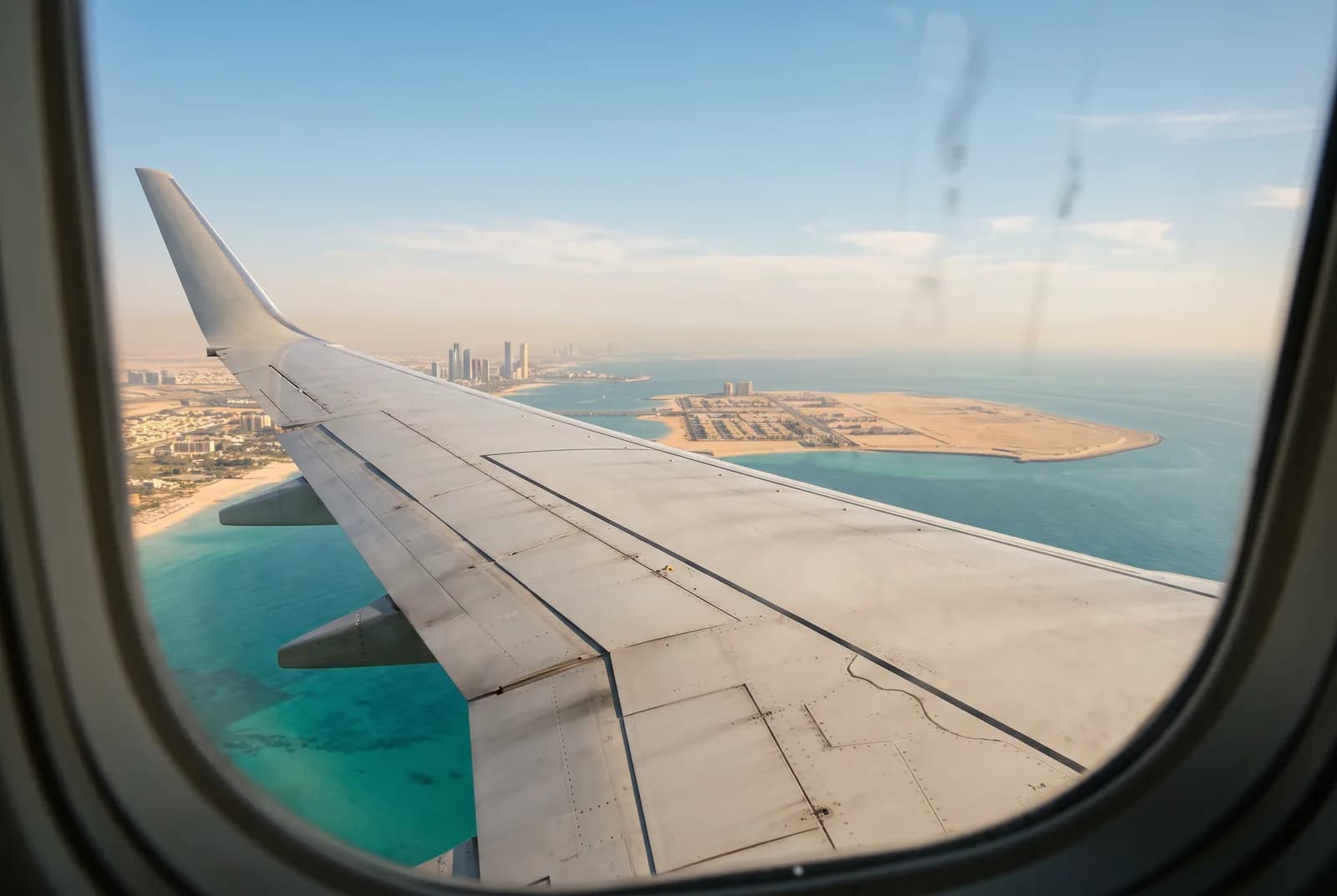 Vista da janela de um avião: uma asa sobre água turquesa e uma ilha de areia